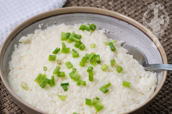 Serving bowl of queso blanco rice with green onions sprinkled on top.