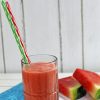 Picture showing Apple Watermelon Smoothie in a glass with two straws and cut watermelon in background.