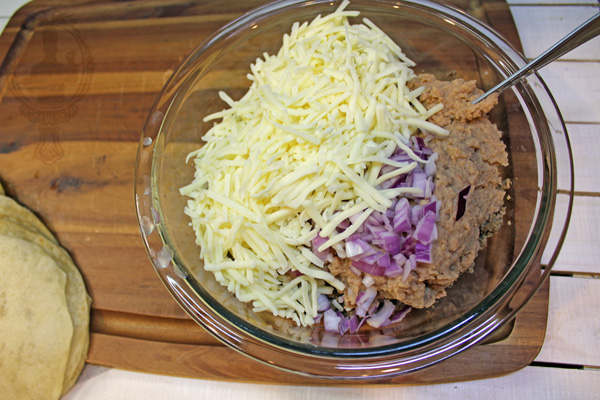 Bowl with refried beans, browned ground beef, cheese and onions.