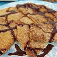Close up of sopapillas on a plate with chocolate syrup drizzled on top.