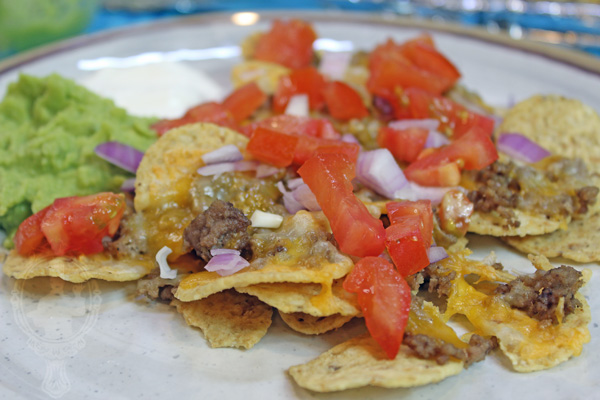 Plate of sheetpan beef nachos with nacho toppings like onions, tomatoes, sour cream and guacamole.