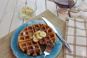 Overhead view of cinnamon sugar waffles on a blue plate with a bowl of sliced bananas and syrup in the background.