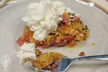 A serving of Hawaiian Dump Cake with whipped cream. A bite waiting on a fork to be devoured.