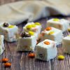 Angle view of Reeses Pieces White Chocolate Fudge with Reeses Pieces candy scattered around.