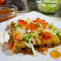 Direct view of a square piece of taco pizza on a plate with sour cream and guacamole on the sides.
