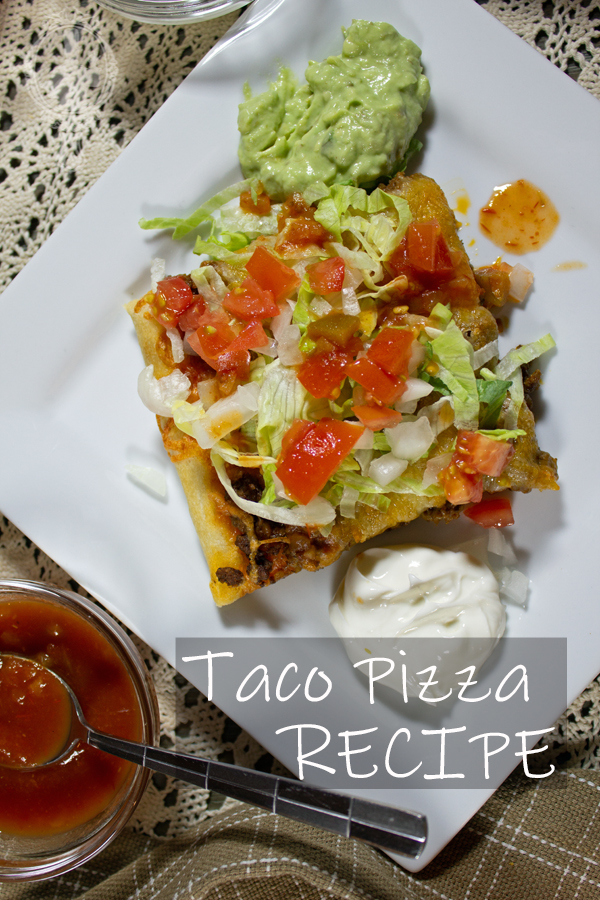 Overhead view of a piece of taco pizza with lettue, tomato and onion on top. Sour cream and guacamole on the side.