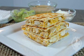 Direct view of a stack of chicken quesadillas on a white plate with extras in the background.
