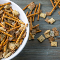 Overhead view of a bowl of ranch snack mix with some spilled out on the table.