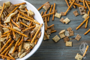 Overhead view of a bowl of ranch snack mix with some spilled out on the table.