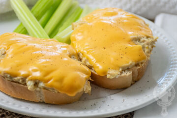 Two slices of tuna melt on a plate with celery sticks.