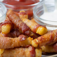 Close up of a serving of bacon fries with condiments on the side.
